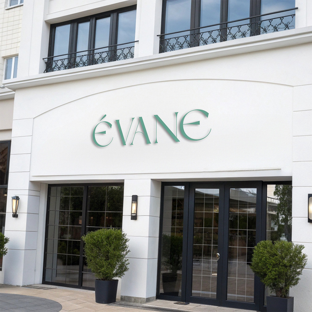 Elegant green "ÉVANE" logo in sophisticated serif typography on modern white building facade above glass entrance doors with potted plants, showcasing luxury beauty salon branding