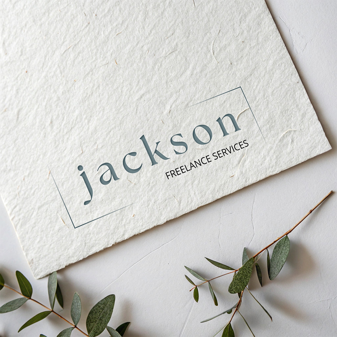 Minimalist "Jackson Freelance Services" logo in soft blue serif typography with subtle geometric frame on textured handmade paper mockup accompanied by eucalyptus branches